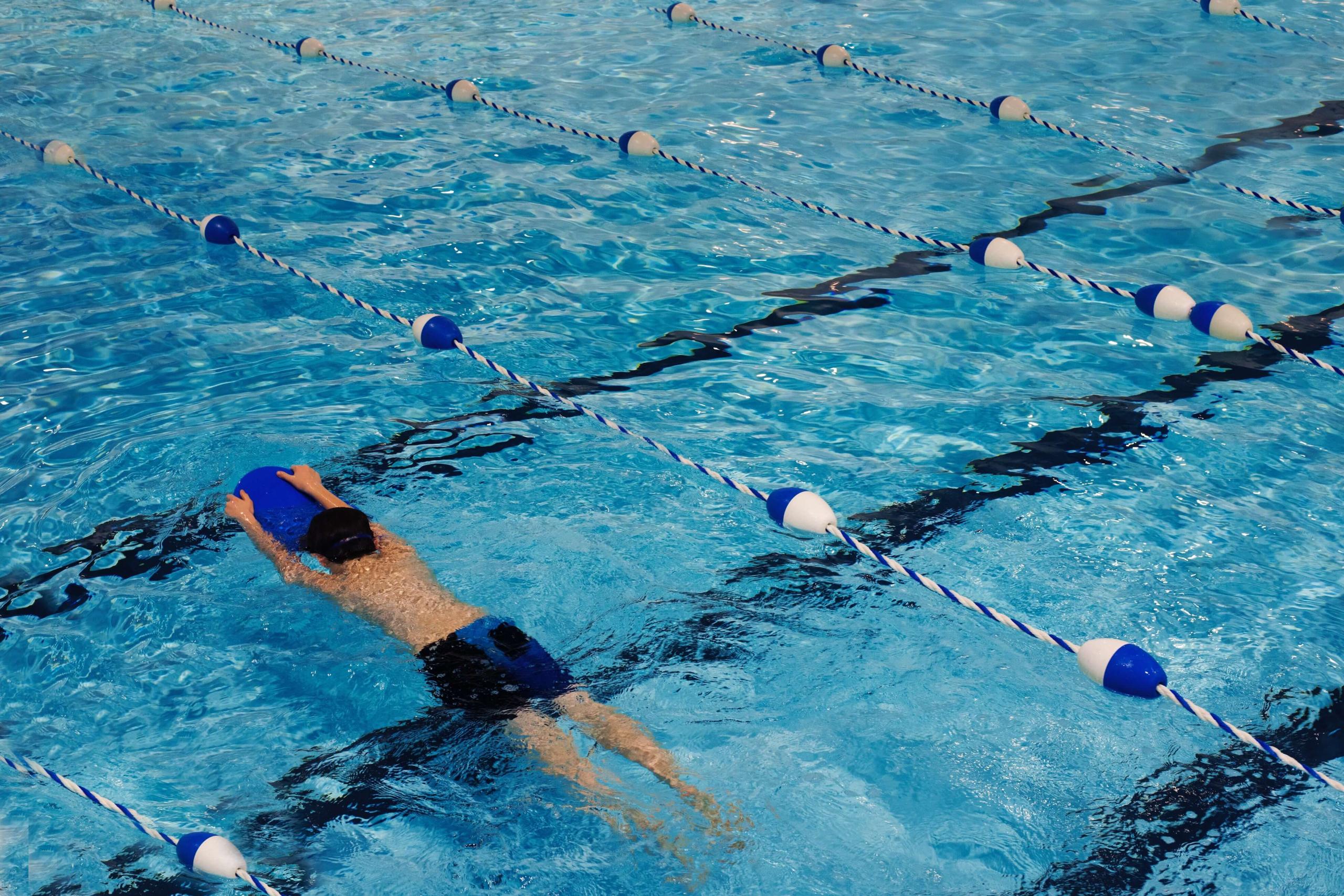 A swimmer holding a kickboard crossing a marked training lane in a pool